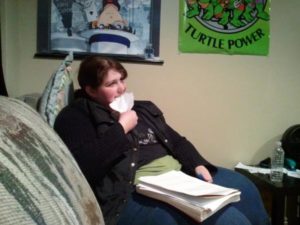 Middle grade author and illustrator Melissa Douglas eating a printed rejection letter while sitting on a couch, a stack of manuscript pages in her lap
